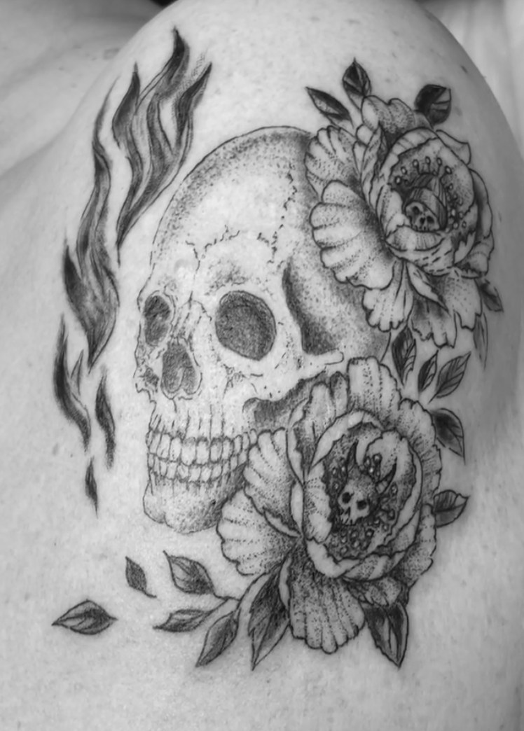 Schädel mit Blüten und Blättern als Tattoo auf einer Schulter.