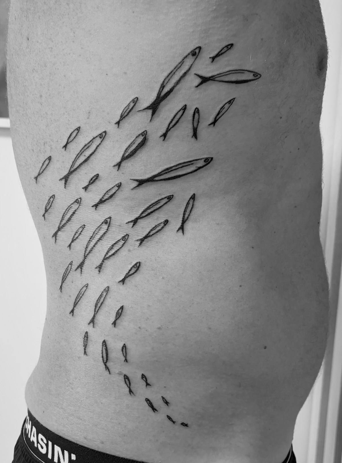 Schwarm stilisierter Fische als Tattoo an der Körperseite.