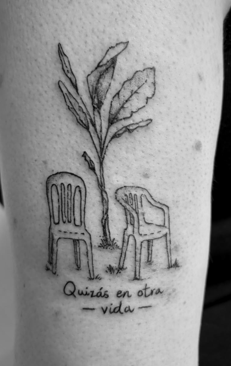 Zwei leere Stühle unter einem wachsenden Zweig mit dem Schriftzug Quizás en otra vida als Tattoo.